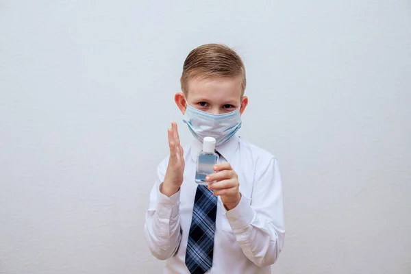 Een gemaskerde jongen in een wit shirt en stropdas heeft een alcohol ontsmettingsmiddel. — Stockfoto