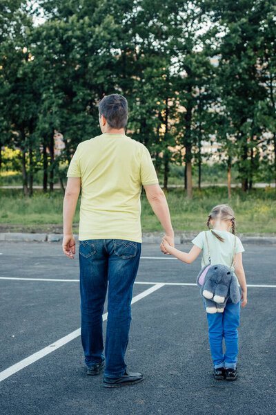 Папа и дочь идут по улице в легкой одежде, на девушке рюкзак
