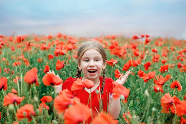 Dívka evropského vzhledu se dvěma náušnicemi v červených šatech stojí v krásném makovém poli proti — Stock fotografie