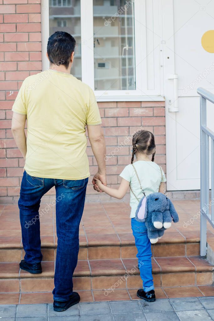 Dad and daughter are standing against the background of a building or House with their backs.