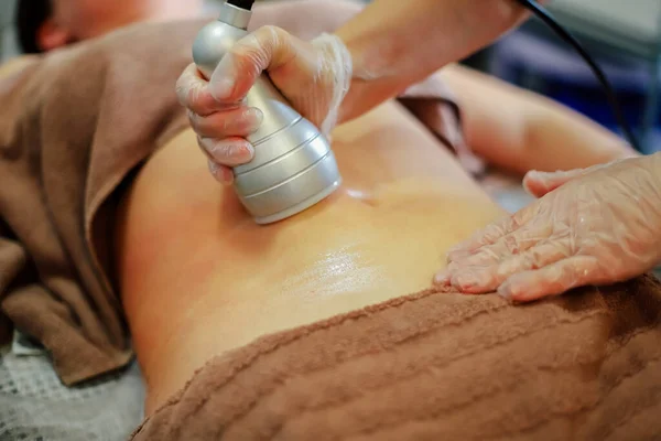 Hands of a person doing a cellulite removal procedure on womans stomach