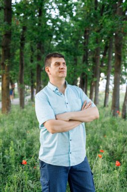 Orta yaşlı bir adam bir ağacın yanında durur ve gülümser. yeşilliğin arka planına karşı