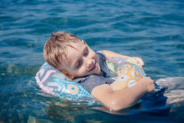 Plavovlasý chlapec leží v nafukovacím kruhu a koupe se v moři — Stock fotografie