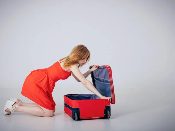 Ein junges Mädchen im roten Kleid blickt in einen offenen Koffer und stellt Dinge zusammen — Stockfoto