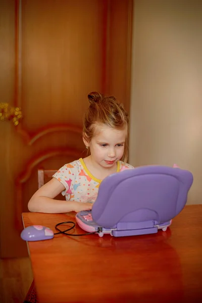 Κορίτσι κάθεται στο τραπέζι και κοιτάζει το μωβ υπολογιστή — Φωτογραφία Αρχείου