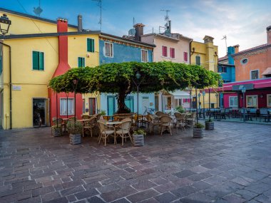 Ağacın altında masası olan bir sahil köyünün meydanı.