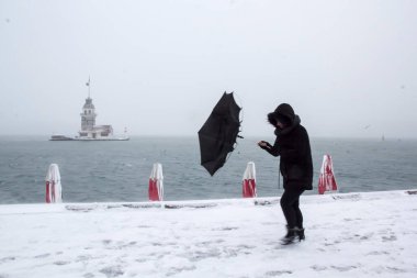 Bakire Kulesi (Kiz Kulesi) karlı kış ve İstanbul, Türkiye 'den insanlar şemsiyeyle yürüyor