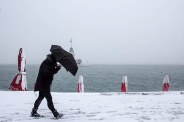 Maiden's Tower (Kiz Kulesi) winter with snow and people is walking with umbrella from Istanbul, Turkey clipart