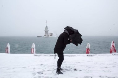 Bakire Kulesi (Kiz Kulesi) karlı kış ve İstanbul, Türkiye 'den insanlar şemsiyeyle yürüyor