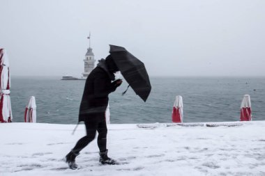 Bakire Kulesi (Kiz Kulesi) karlı kış ve İstanbul, Türkiye 'den insanlar şemsiyeyle yürüyor