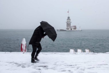 Bakire Kulesi (Kiz Kulesi) karlı kış ve İstanbul, Türkiye 'den insanlar şemsiyeyle yürüyor