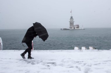 Bakire Kulesi (Kiz Kulesi) karlı kış ve İstanbul, Türkiye 'den insanlar şemsiyeyle yürüyor