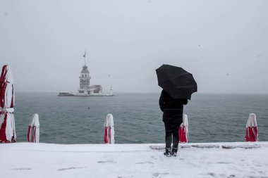 Bakire Kulesi (Kiz Kulesi) karlı kış ve İstanbul, Türkiye 'den insanlar şemsiyeyle yürüyor