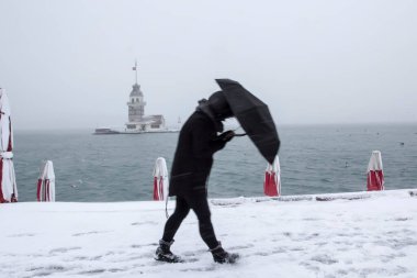 Bakire Kulesi (Kiz Kulesi) karlı kış ve İstanbul, Türkiye 'den insanlar şemsiyeyle yürüyor