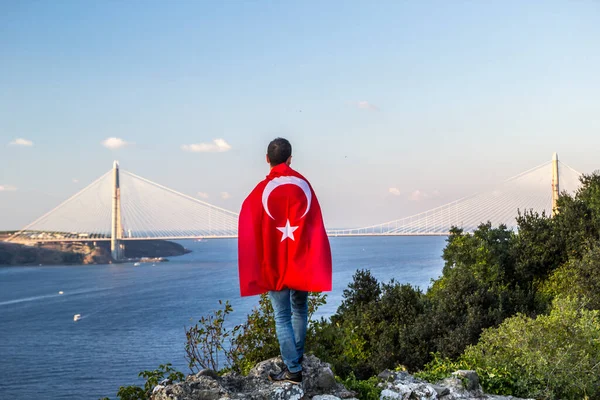 トルコの旗を持った男が海に架かる橋を眺め ストック写真
