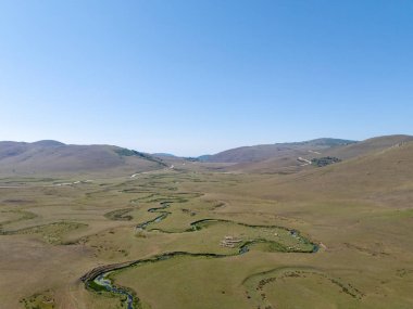 Türkiye 'nin Ordu kentindeki Persembe Platosu' nda havadan seyyar yılan manzarası. Geleneksel köy evleri olan yemyeşil bir vadiden akan dolambaçlı bir nehir. Açık bir yaz gökyüzü altında Karadeniz dağlarının çarpıcı coğrafi örüntüsü.