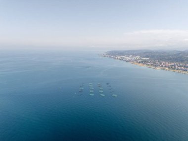 Türkiye 'nin Trabzon kentinin Arsin kıyısındaki deniz ürünleri kafeslerinin insansız hava aracı panoraması. Kentsel yerleşimlerin görüldüğü Karadeniz kıyı şeridi, modern deniz tarım ve sürdürülebilir deniz ürünleri üretimini vurguluyor.
