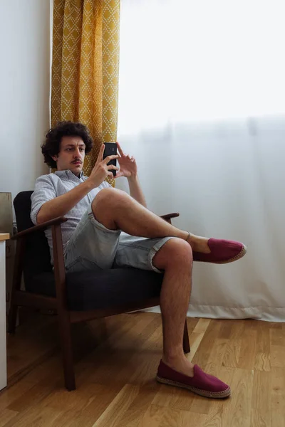 Красивый Молодой Человек Сидящий Кресле Мобильным Телефоном Руке Покупающий Онлайн — стоковое фото