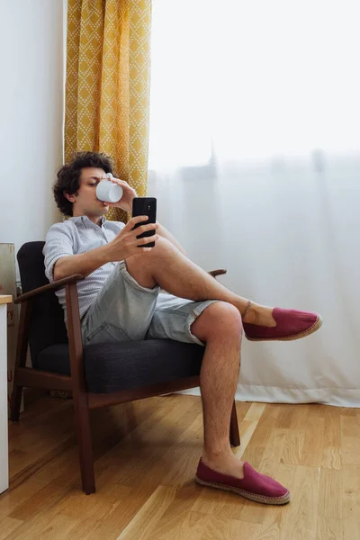 Ελκυστικός Νεαρός Άνδρας Που Τηλεργάζεται Ένα Κινητό Τηλέφωνο Κάθεται Σταυροπόδι — Φωτογραφία Αρχείου