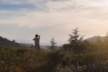 Şehirden uzakta tatildeyken dağda gün batımına bakan hoş bir kadın. Seçici odak.