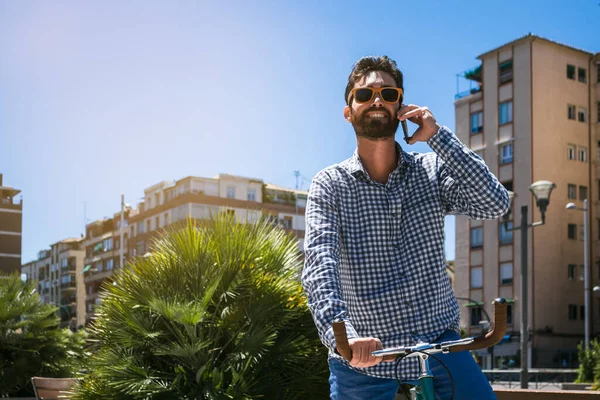 Handsome man with sunglasses smiling and talking on the mobile phone. Fixed Gear bicycle. Outdoor horizontal photography.