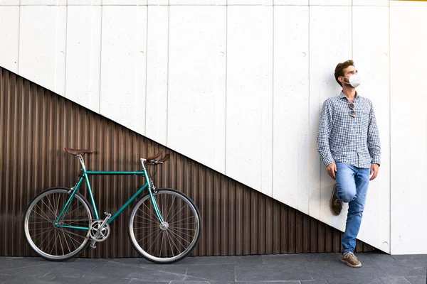 Attractive man with mask with fixed gear bicycle standing on a two-color modern wall. Coronavirus period. Horizontal photography, hipster style.
