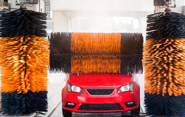 Car wash, red car in automatic car wash, rotating yellow and blue brush. Washing vehicle.