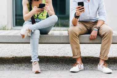 Üniversite bankında oturan genç bir çiftin cep telefonlarına baktığı yakın çekim.