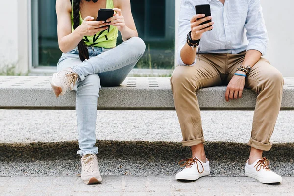 Üniversite bankında oturan genç bir çiftin cep telefonlarına baktığı yakın çekim.