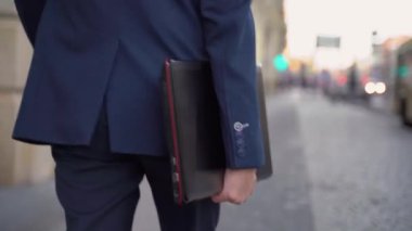 Elinde dizüstü bilgisayarla caddede yürüyen yakın plan iş adamı. Dizüstü bilgisayar elinde.