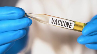 Mikrobiyolog ya da tıp çalışanı elinde yazıt aşısı olan bir ampul tutuyor. Coronovirüs aşısı. Mavi cerrahi eldivenli doktor Covid-19 aşısının icadı.