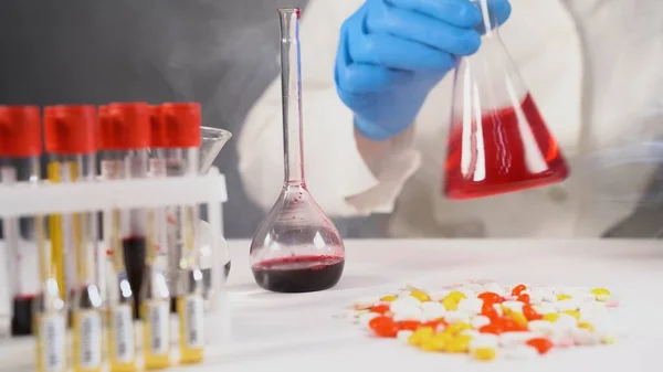 Chemist or medicine holding and looking at a glass flask while a chemical reaction is underway. Testing samples for presence of virus COVID-19. Smoke on background