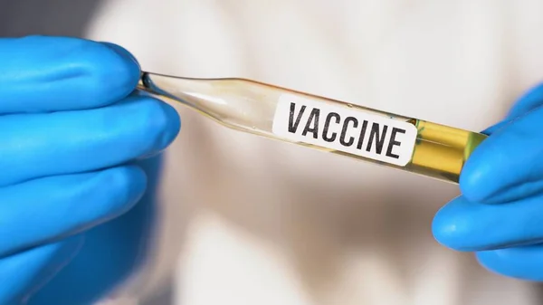 Microbiólogo o trabajador médico sostiene una ampolla con la vacuna de inscripción en la mano. Vacuna contra el Coronovirus. Médico en guantes quirúrgicos azules invención de la vacuna Covid-19 — Foto de Stock
