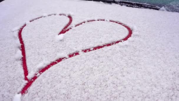 Cuore disegnato con le dita nella neve. Cuore rosso dipinto sul cofano innevato. Il cofano dell'automobile in inverno nevoso. Chiudere, disegnare cuori sulla macchina coperta di neve. Bel simbolo del cuore disegnato — Video Stock