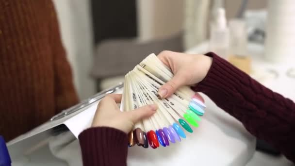 Vrouwen handen kiezen spijkermonster uit het plastic palet. Meisje hand kiezen nagel kleur tester in nagel salon. Mooie handen en collectie van nagel monsters. — Stockvideo