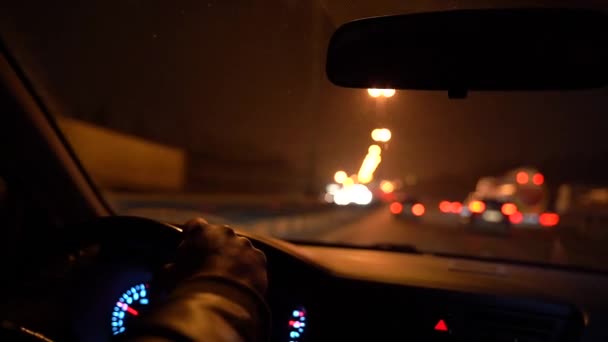 Handen op het stuur van de auto. Nachtelijke auto rijden in het verkeer op de snelweg. Stuurwiel en bestuurder handen, auto dashboard. Onduidelijke contouren van het verkeer. — Stockvideo