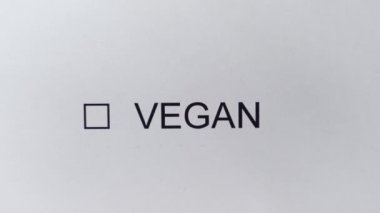 VEGAN - Erkek eli beyaz kağıt kalem ile işaretli kutuya bir kene çizer. VEGAN yazısıyla işaretleme kutusu. Diyet, vejetaryen yaşam tarzı, ekolojik ürünler, organik.