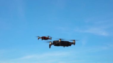 Mavi gökyüzüne karşı uçan iki kuadkopter. Çerçevede uçan iki dron. İnsansız hava aracı kamerasıyla uçmak ve çekim yapmak