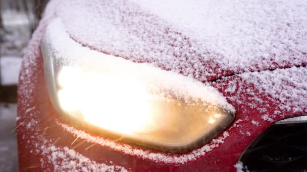 Światła samochodowe w śnieżnej zimie. Reflektor samochodu z bliska w dzień opadów śniegu, oświetlenie samochodowe, burza śnieżna na zewnątrz — Wideo stockowe