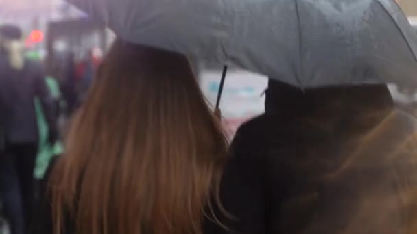 Några under ett paraply som går nerför gatan där. Ungdomar går under paraplyet under regnet. — Stockvideo