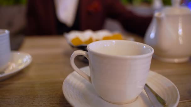 Homme d'affaires assis à une table dans un café verser le thé dans une tasse blanche. Homme mains avec théière blanche dans le restaurant. Un homme pur thé d'une bouilloire dans une tasse blanche sur une table en bois 