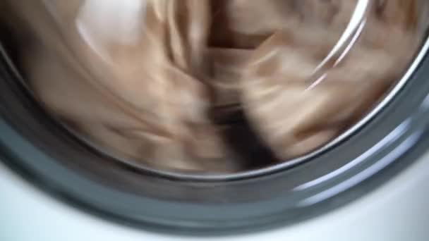 Closeup bottom of the glass door of the washing machine. Clothes rotate counterclockwise in a chrome drum from right to left — Stock Video