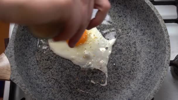 Chef seasons a Frying egg, sunny side up, with ground pepper in a small frying pan over an gas burning stove — Stock Video