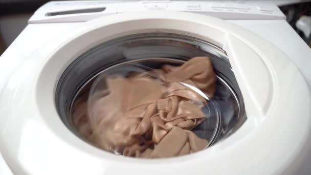 Kleidungsstücke drehen sich in der Chromtrommel gegen den Uhrzeigersinn von rechts nach links. Die Waschmaschine ist in Bewegung. Frontansicht von unten, eine ungewöhnliche Perspektive — Stockvideo