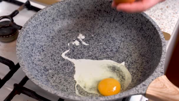 Mãos de homem de close-up quebrar dois ovos sobre a frigideira. Cozinhar ovo em uma pequena frigideira sobre um fogão a gás. Dois ovos são rachados e fritos na superfície quente da panela — Vídeo de Stock