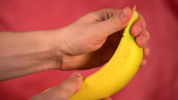 男は赤い背景にきれいなバナナを手。バナナの皮をむいて — ストック動画