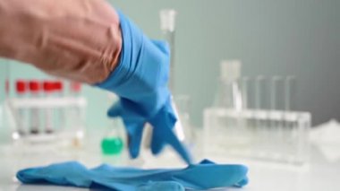 Doktor mavi lateks eldiven giyer. Bilim adamı, laboratuvar masasının arka planına eldiven takıyor. Koronovirüsten korunma