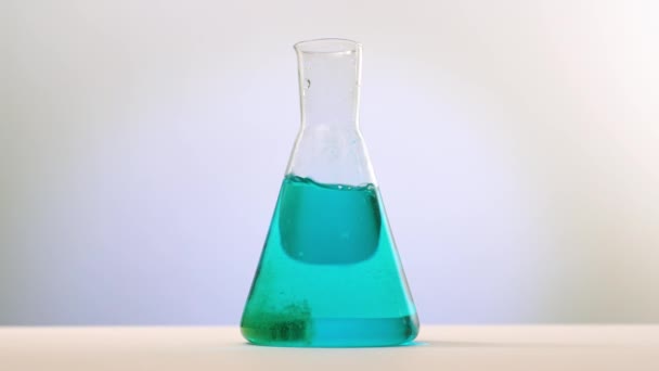 La compressa viene gettata e si scioglie in un pallone di vetro con liquido blu. La reazione chimica blu è colorata di verde — Video Stock