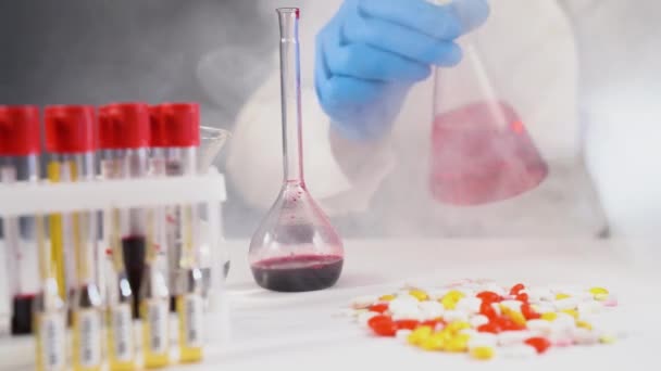 Chemik nebo lék drží skleněnou baňku a dívá se na ni, zatímco probíhá chemická reakce. Testování vzorků na virus COVID-19 — Stock video