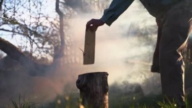 Odun kesen bir adam. Duman arkaplanındaki baltayla tahtayı keser